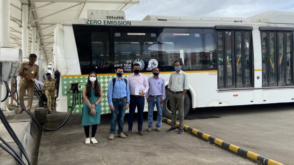 group in front of an electric bus that is plugged into a charger in Pune, India