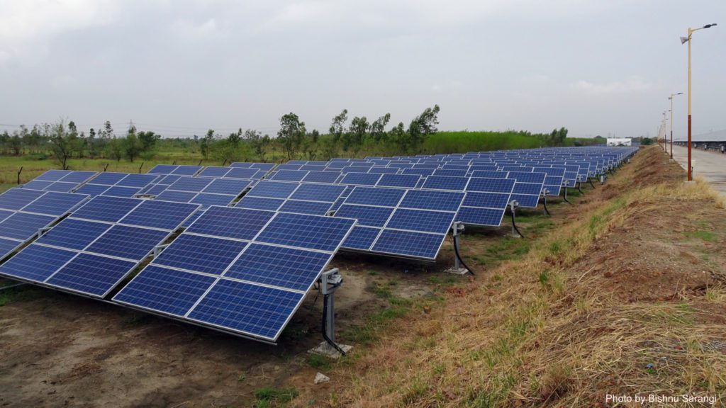 rows of blue solar panels on a field beside road in India