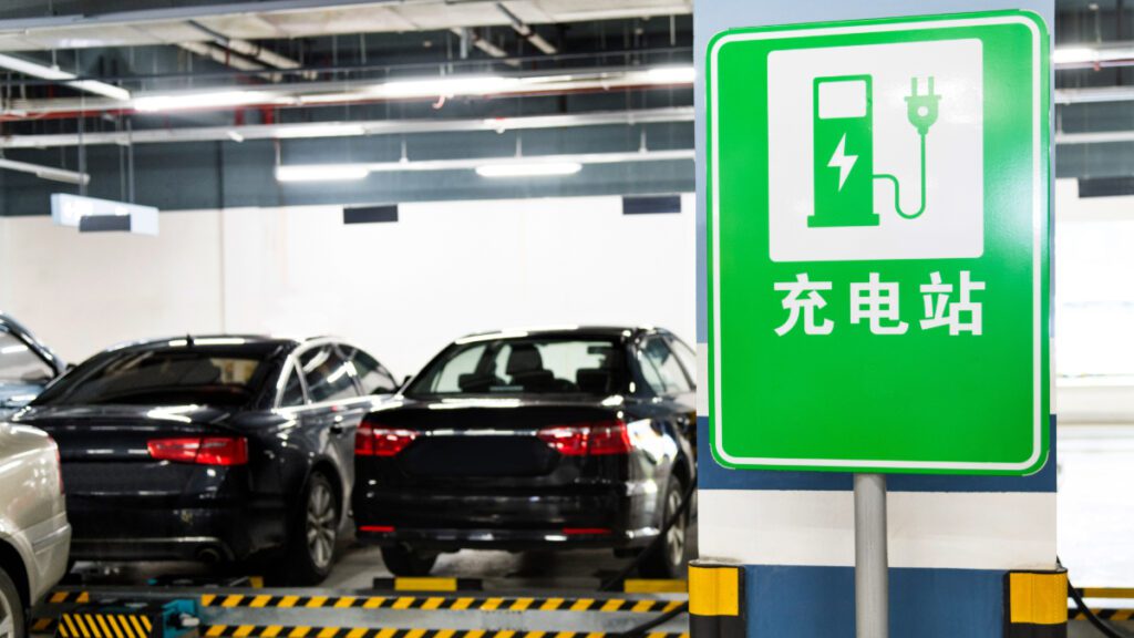 Indoor parking garage with two black sedans in the background and a green signed for an EV charger in the foreground with writing in Chinese